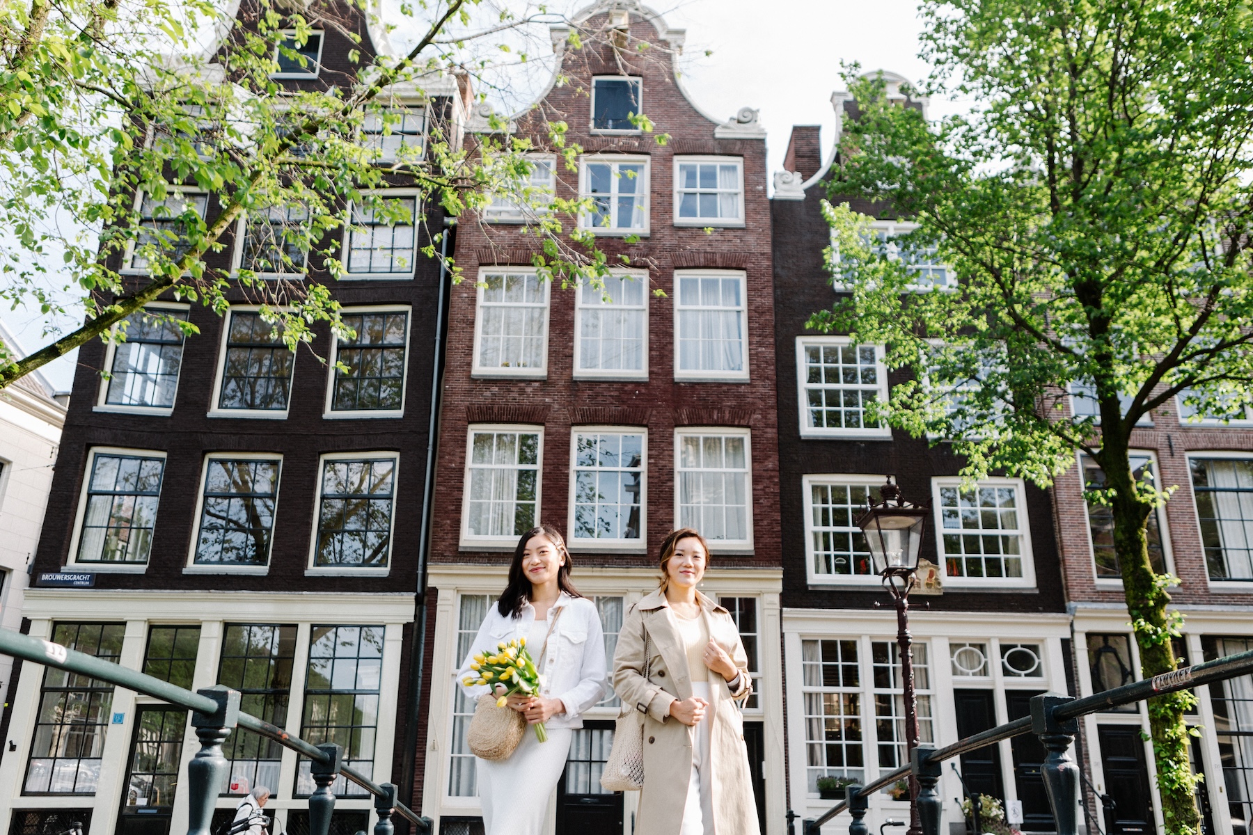 Two women walk across a bridge holding flowers in Amsterdam.